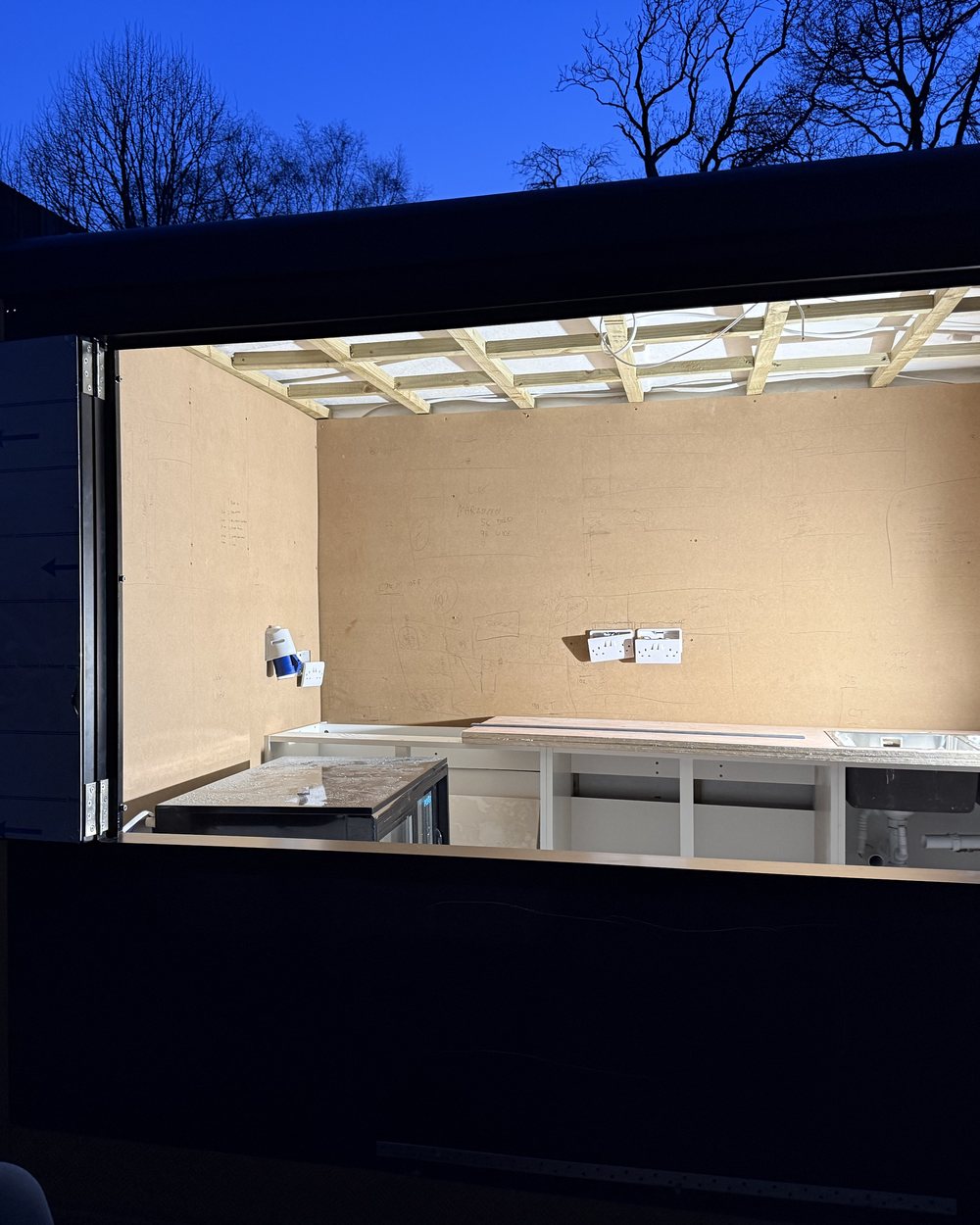 A unit opened up at dusk: bare walls, ceiling battens and sockets, with the layout drawn on the board