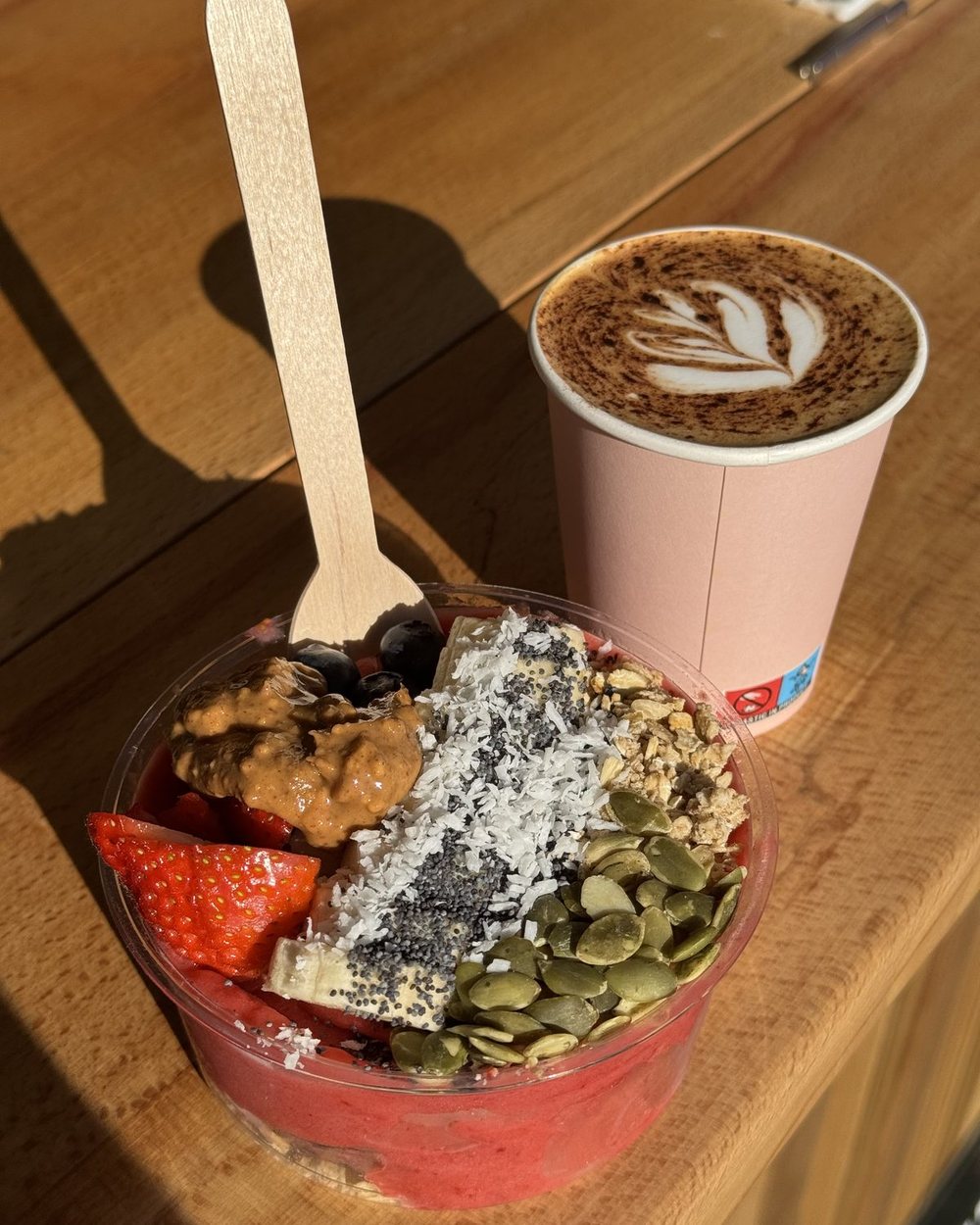 An açaí bowl with strawberries, granola and pumpkin seeds beside a latte