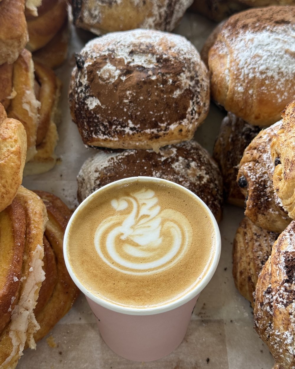 A swan latte surrounded by fresh pastries