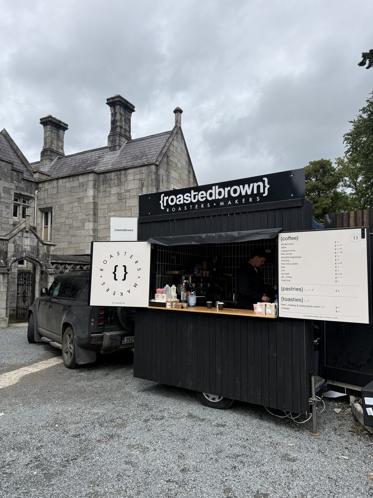 Roasted Brown trailer, black and timber, parked in front of a stone building
